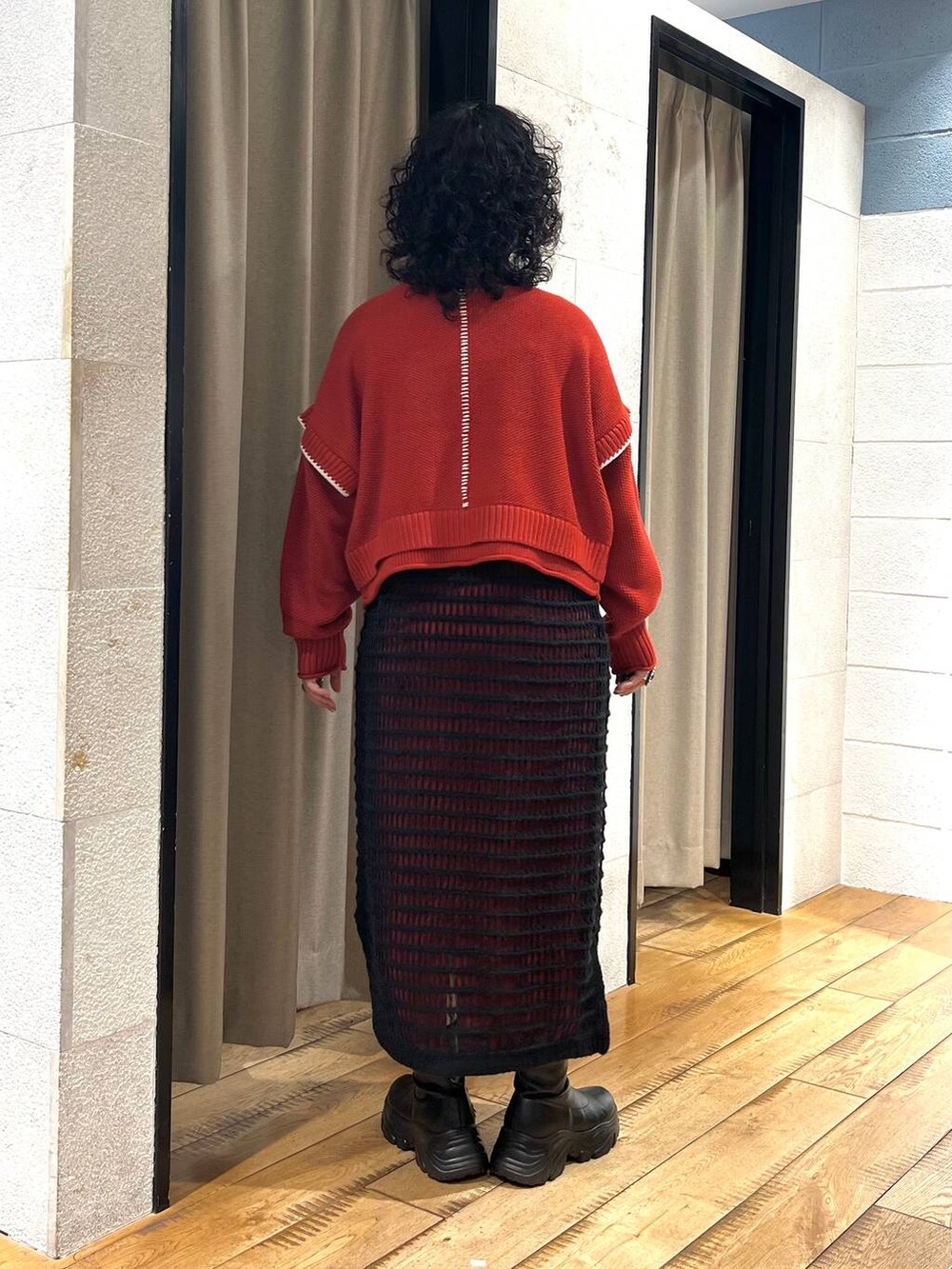 レッド系のニット/セーター、ブラック系のブーツ、ブラック系のワンピースを着用したレディースの秋コーディネートの3枚目の写真
