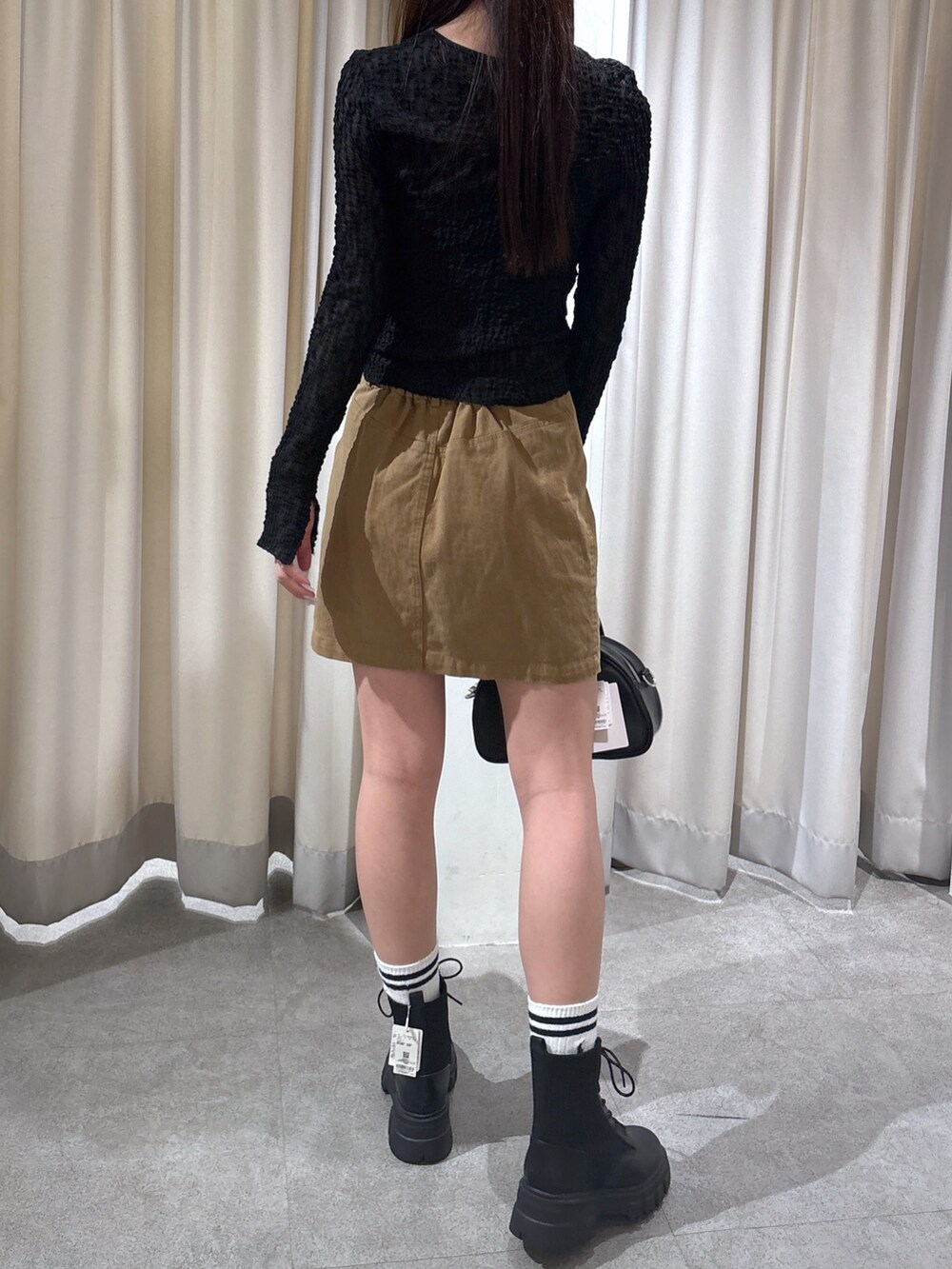 ベージュ系のスカート、ブラック系のカーディガン/ボレロ、ブラック系のトートバッグを着用したレディースの春コーディネートの2枚目の写真