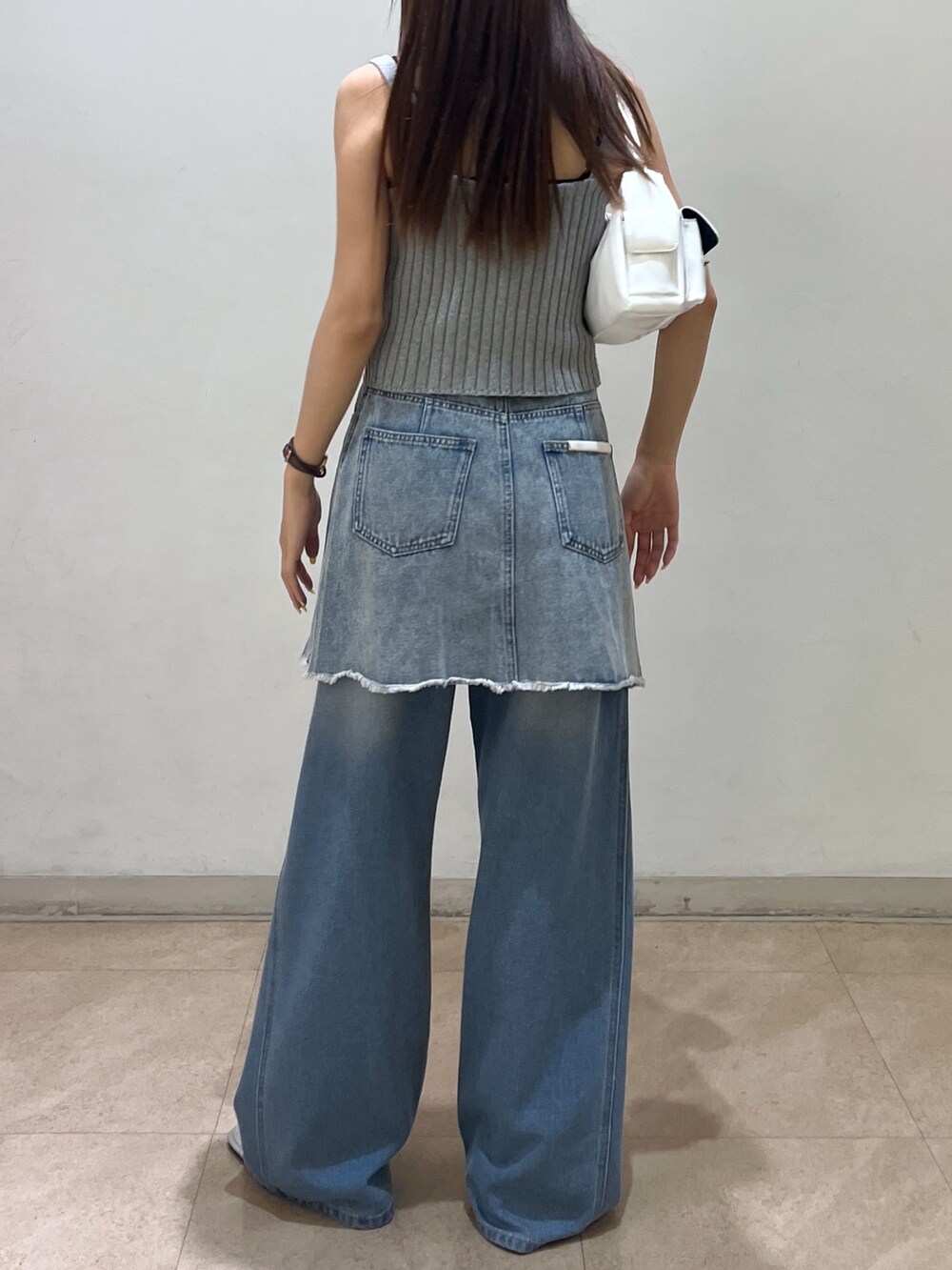 ブルー系のデニムパンツ、ブルー系のスカート、ホワイト系のハンドバッグを着用したレディースの夏コーディネートの2枚目の写真