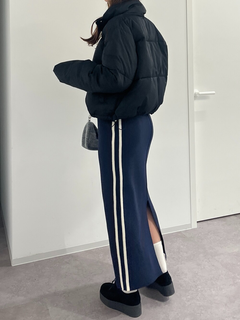 シルバー系のハンドバッグ、ブルー系のスカート、ホワイト系のニット/セーターを着用したレディースの冬コーディネートの2枚目の写真