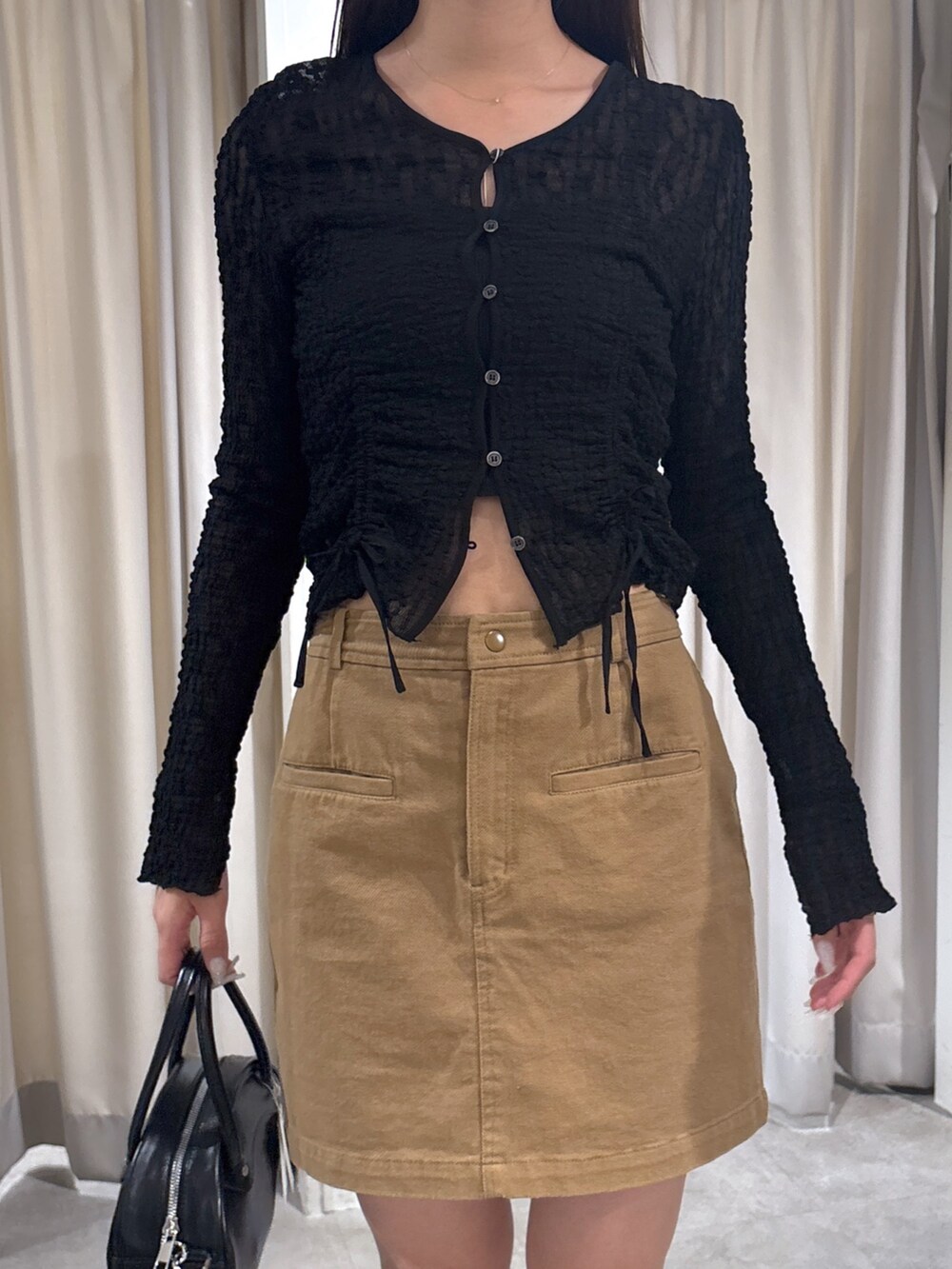 ベージュ系のスカート、ブラック系のカーディガン/ボレロ、ブラック系のトートバッグを着用したレディースの春コーディネートの3枚目の写真