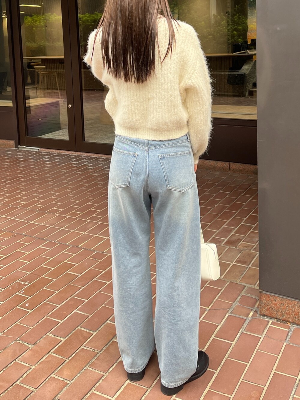 ブルー系のデニムパンツ、ホワイト系のショルダーバッグ、ホワイト系のニット/セーターを着用したレディースの冬コーディネートの2枚目の写真