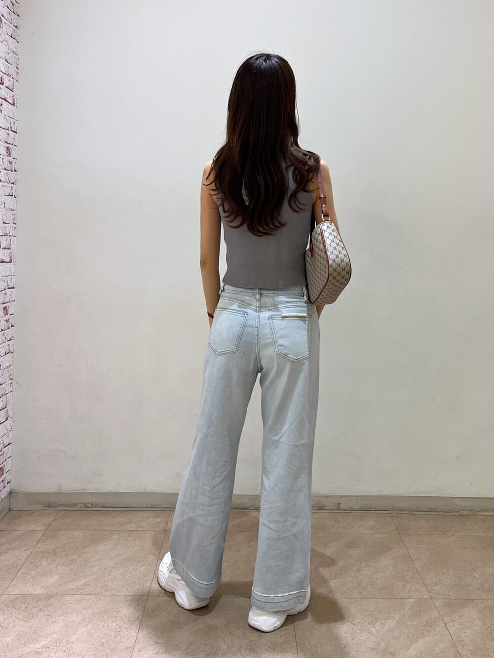 ブルー系のデニムパンツ、ベージュ系のショルダーバッグ、グレー系のニット/セーターを着用したレディースの夏コーディネートの2枚目の写真