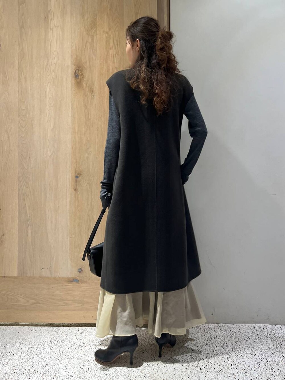 グレー系のベスト、グレー系のニット/セーター、ホワイト系のスカートを着用したレディースの秋コーディネートの4枚目の写真