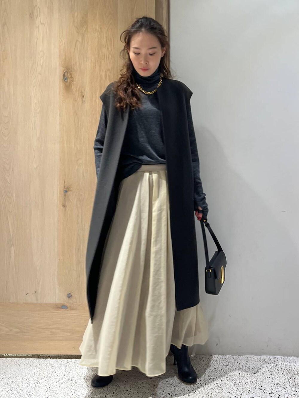 グレー系のベスト、グレー系のニット/セーター、ホワイト系のスカートを着用したレディースの秋コーディネートの2枚目の写真