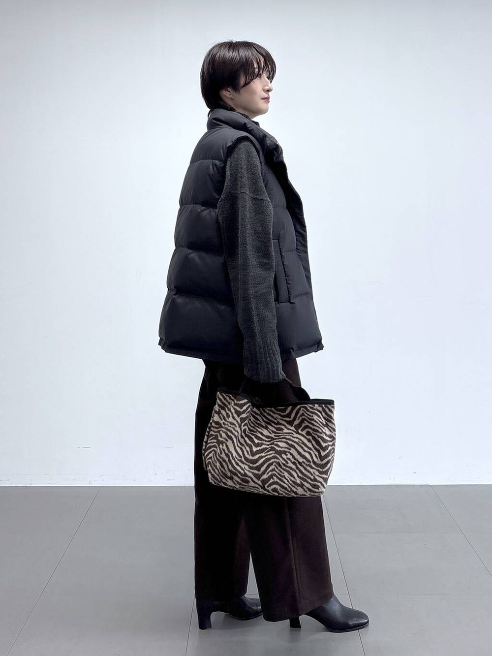 ブラック系のダウンベスト、グレー系のニット/セーター、ブラック系のブーツを着用したレディースの秋コーディネートの3枚目の写真