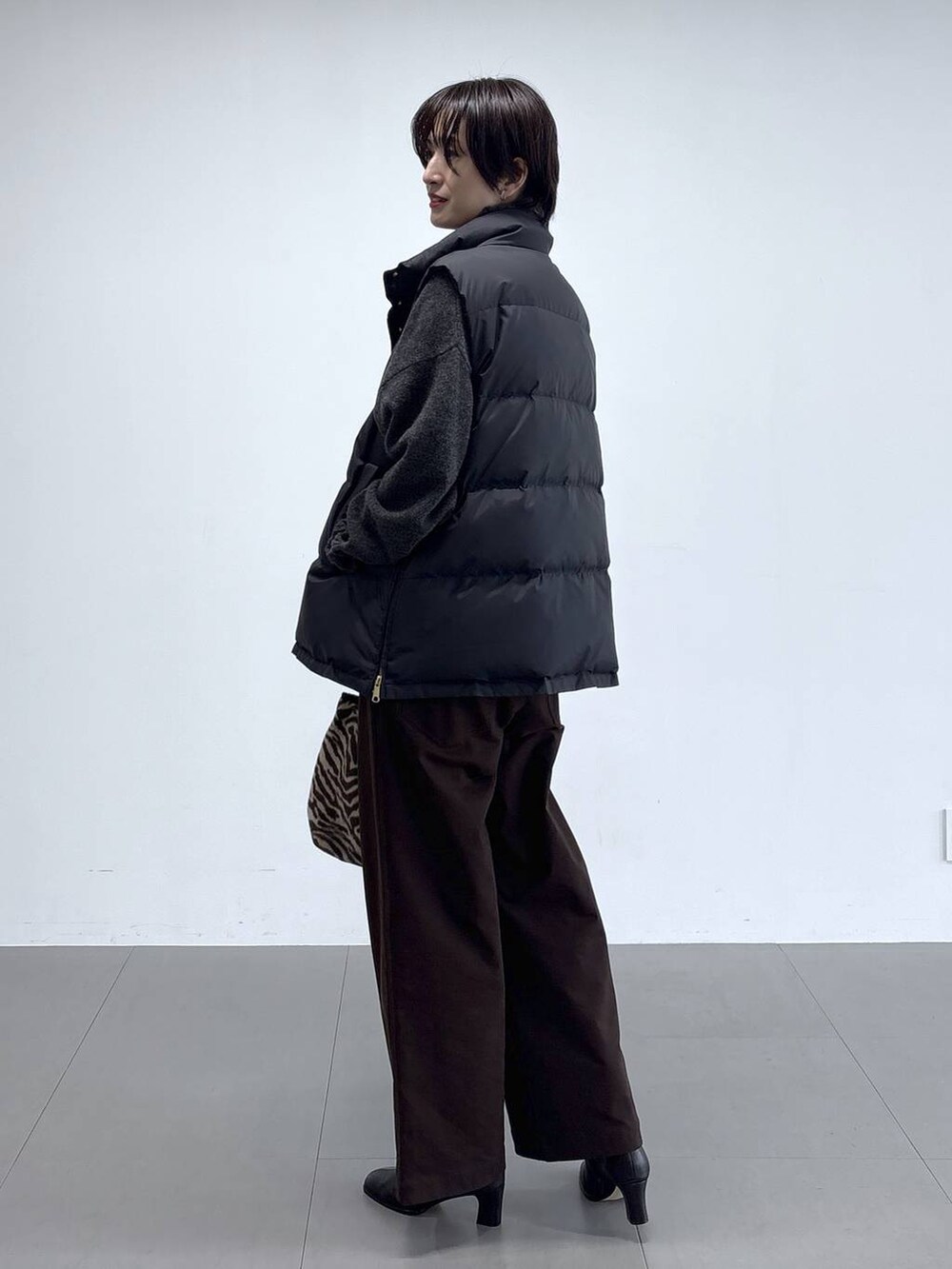 ブラック系のダウンベスト、グレー系のニット/セーター、ブラック系のブーツを着用したレディースの秋コーディネートの2枚目の写真