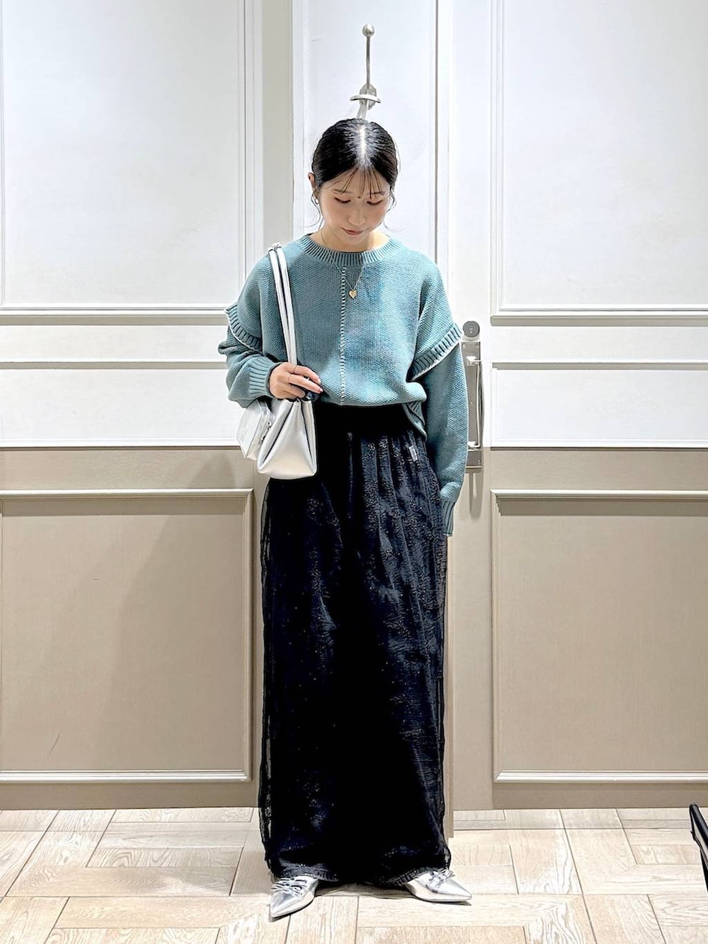 グリーン系のニット/セーター、シルバー系のパンプス、ブラック系のデニムパンツを着用したレディースの秋コーディネートの2枚目の写真