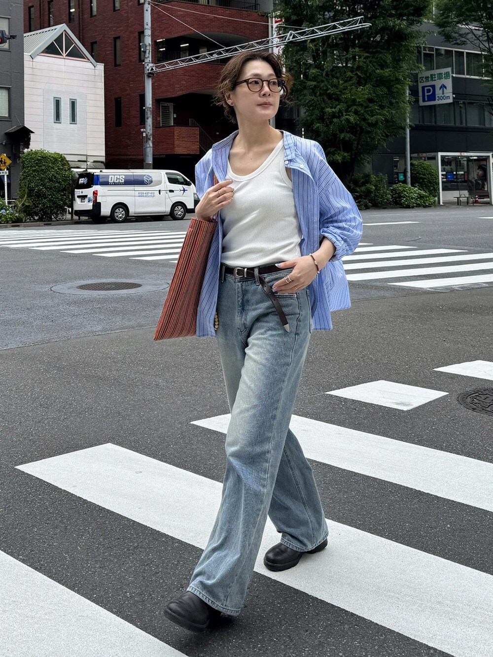 ブルー系のシャツ/ブラウス、オレンジ系のトートバッグ、ブラウン系のブーツを着用したレディースの夏コーディネートの2枚目の写真