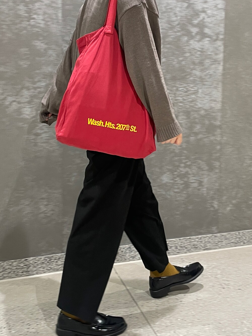 グレー系のニット/セーター、ブラック系のスラックス、レッド系のトートバッグを着用したメンズの秋コーディネートの3枚目の写真