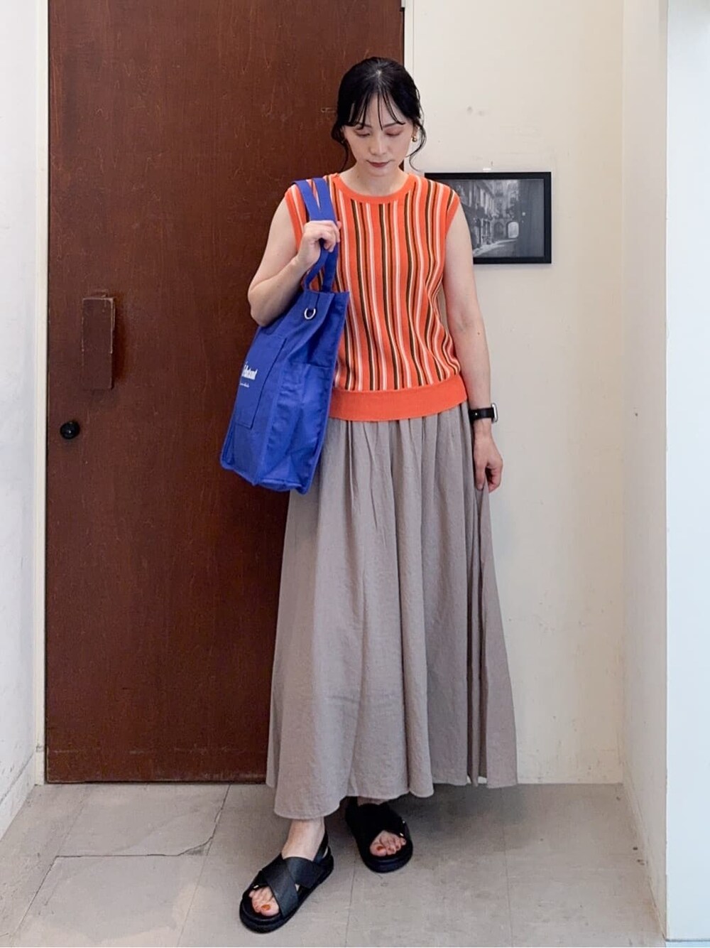 オレンジ系のニット/セーター、ブラウン系のその他パンツ、ブルー系のトートバッグを着用したレディースの夏コーディネートの2枚目の写真