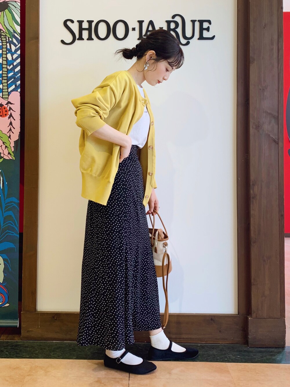 イエロー系のニット/セーター、ブラック系のスカート、ブラウン系のハンドバッグを着用したレディースの春コーディネートの2枚目の写真