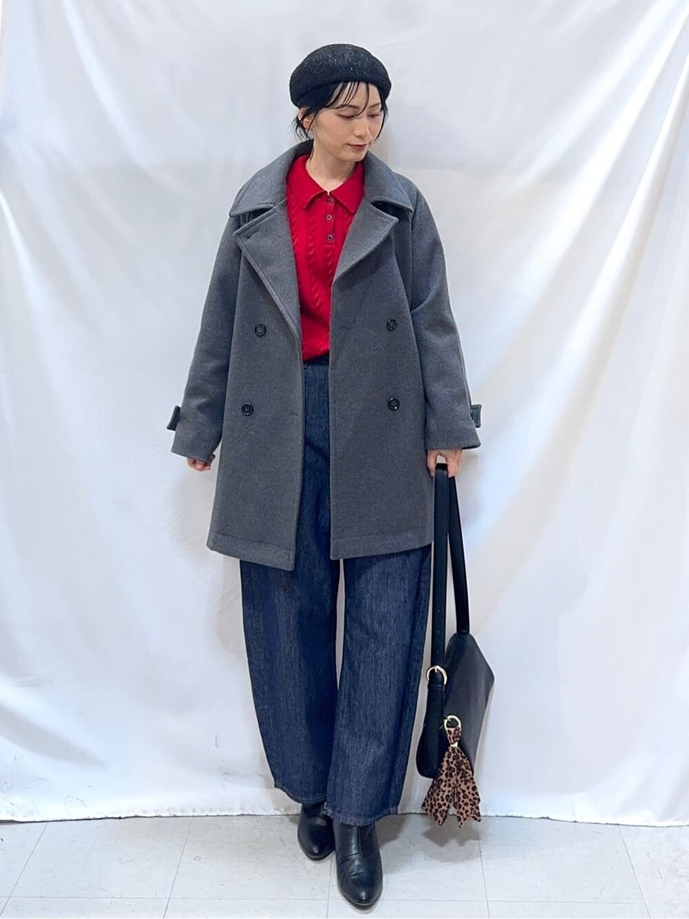 グレー系のチェスターコート、レッド系のニット/セーター、ブルー系のデニムパンツを着用したレディースの冬コーディネートの2枚目の写真