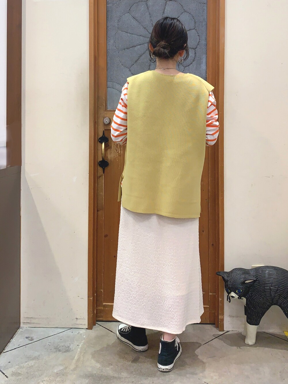 オレンジ系のTシャツ/カットソー、イエロー系のベスト、ホワイト系のスカートを着用したレディースの春コーディネートの3枚目の写真