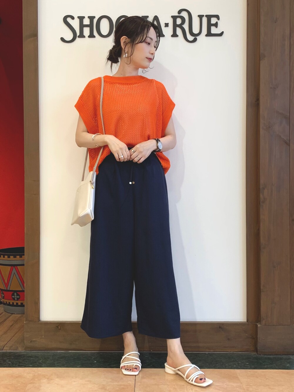 オレンジ系のニット/セーター、ブルー系のその他パンツ、ホワイト系のサンダルを着用したレディースの夏コーディネートの2枚目の写真