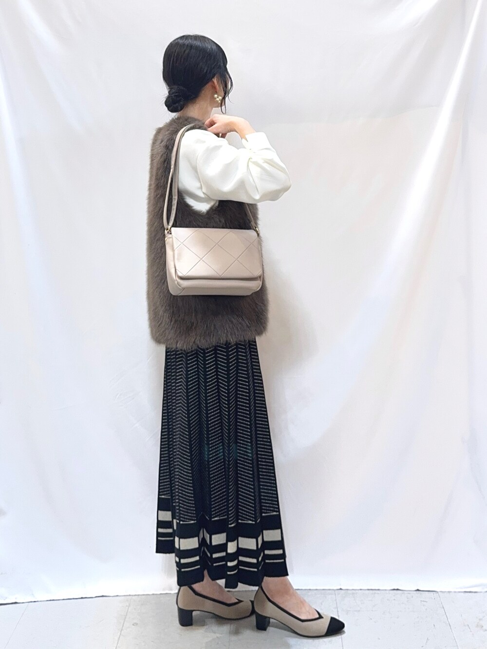 ブラウン系のベスト、ホワイト系のTシャツ/カットソー、ブラック系のスカートを着用したレディースの秋コーディネートの2枚目の写真