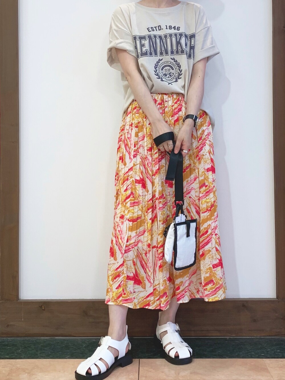 ベージュ系のTシャツ/カットソー、オレンジ系のスカート、ホワイト系のサンダルを着用したレディースの夏コーディネートの2枚目の写真