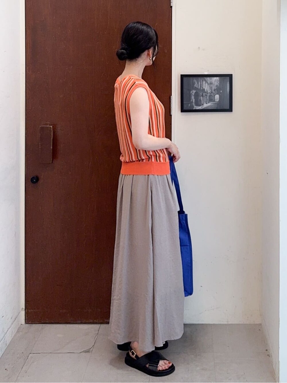 オレンジ系のニット/セーター、ブラウン系のその他パンツ、ブルー系のトートバッグを着用したレディースの夏コーディネートの3枚目の写真