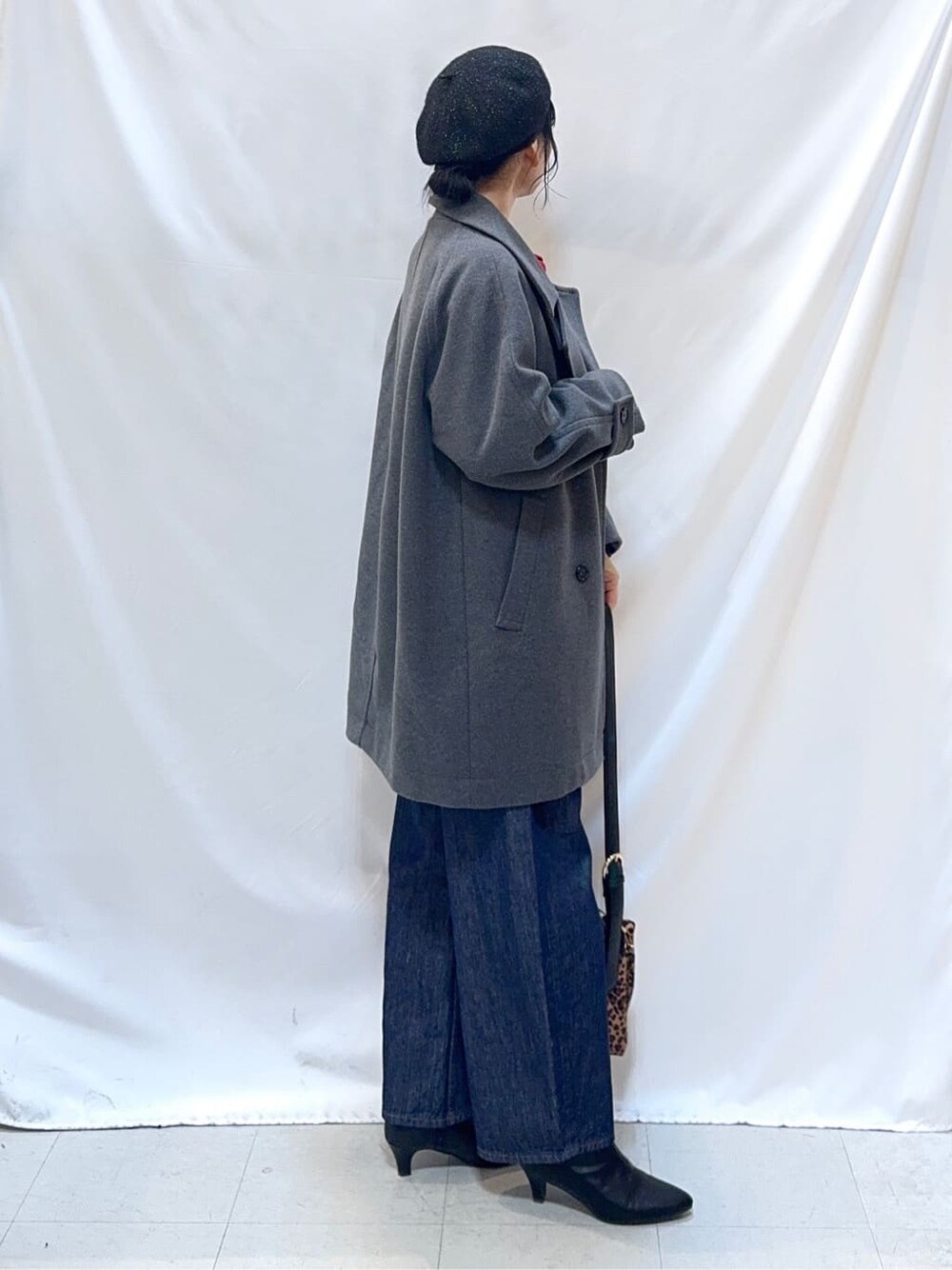 グレー系のチェスターコート、レッド系のニット/セーター、ブルー系のデニムパンツを着用したレディースの冬コーディネートの3枚目の写真