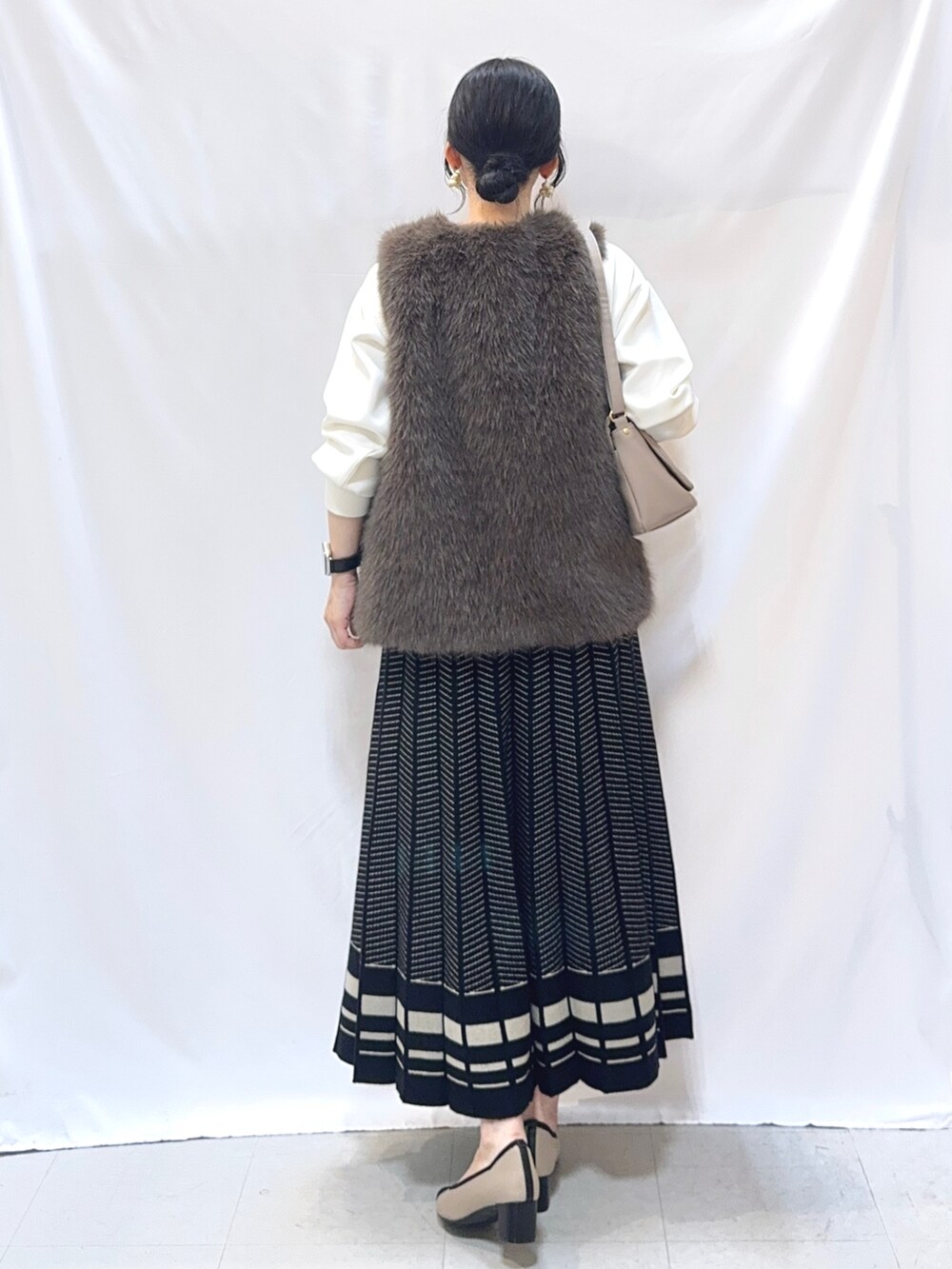 ブラウン系のベスト、ホワイト系のTシャツ/カットソー、ブラック系のスカートを着用したレディースの秋コーディネートの3枚目の写真