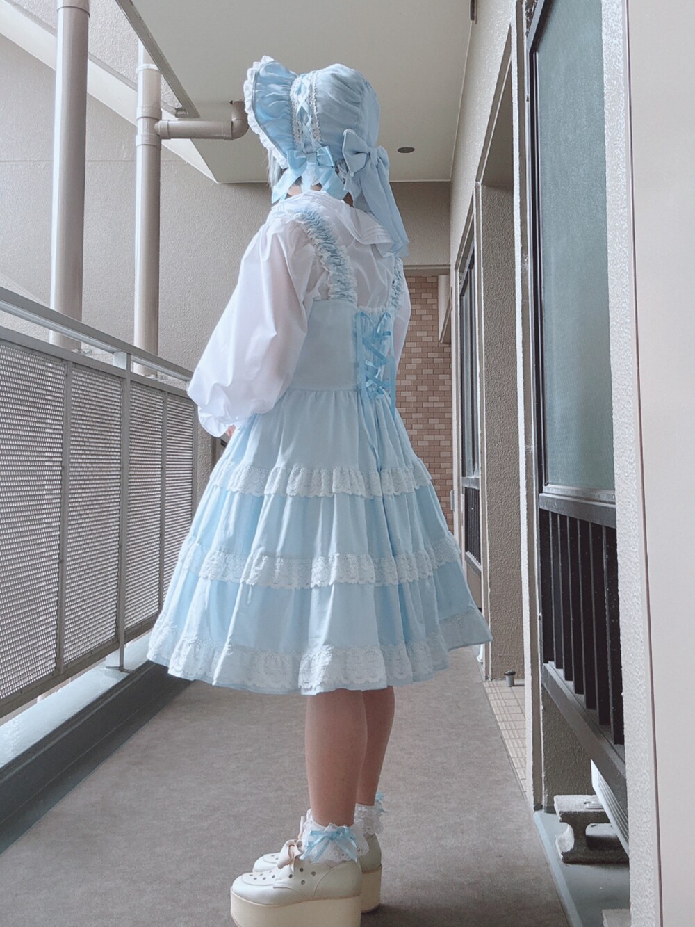 ブルー系のジャンパースカート、ホワイト系のシャツ/ブラウス、ホワイト系のシューズを着用したレディースの春コーディネートの3枚目の写真