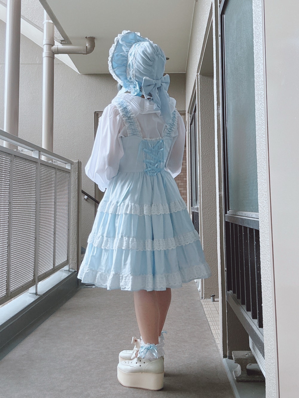 ブルー系のジャンパースカート、ホワイト系のシャツ/ブラウス、ホワイト系のシューズを着用したレディースの春コーディネートの2枚目の写真