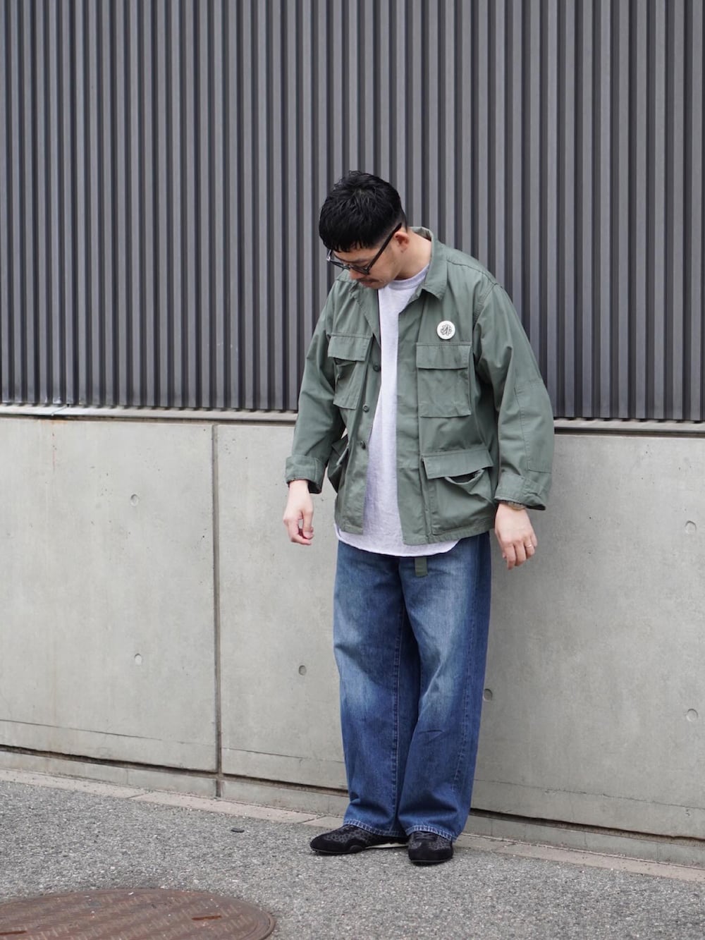 グレー系のTシャツ/カットソー、グリーン系のミリタリージャケット、ブルー系のデニムパンツを着用したメンズの春コーディネートの2枚目の写真