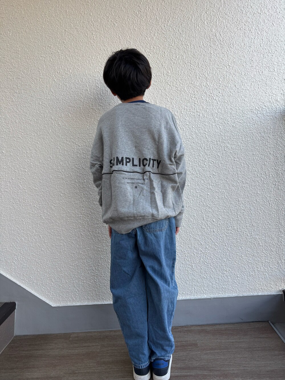 グレー系のスウェット、ブルー系のデニムパンツ、ブルー系のスニーカーを着用したキッズの秋コーディネートの2枚目の写真