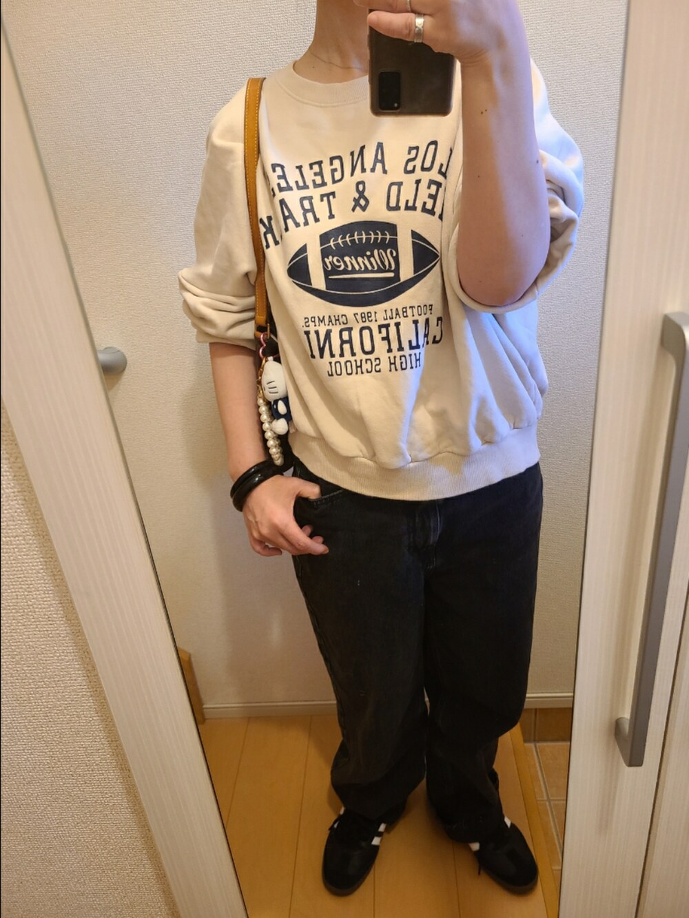 ブラック系のデニムパンツ、ベージュ系のスウェット、ブラウン系のハンドバッグを着用したレディースの秋コーディネートの2枚目の写真