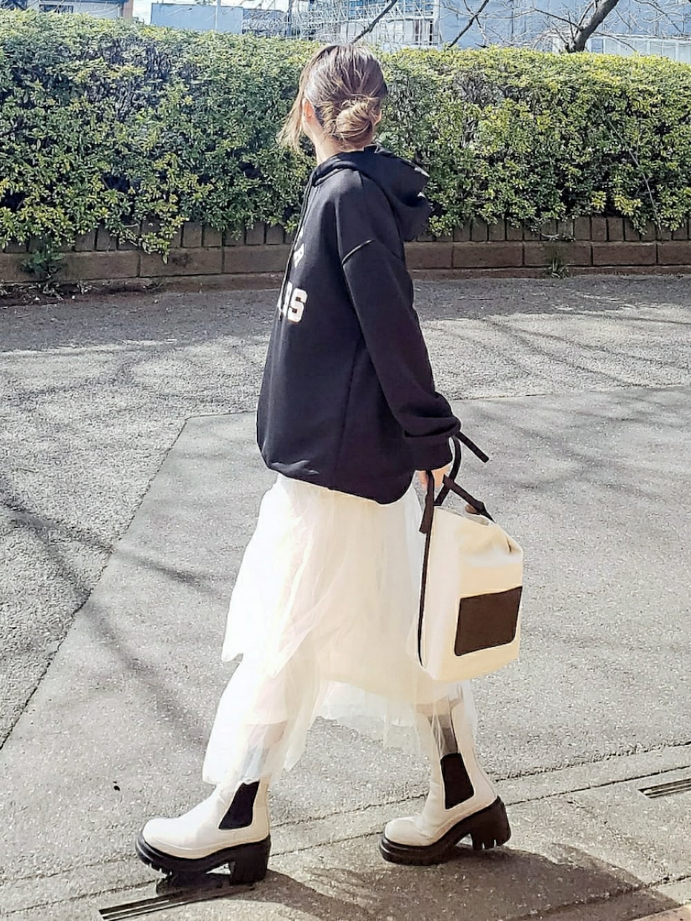ブラック系のパーカー、ホワイト系のスカート、ホワイト系のブーツを着用したレディースの春コーディネートの2枚目の写真