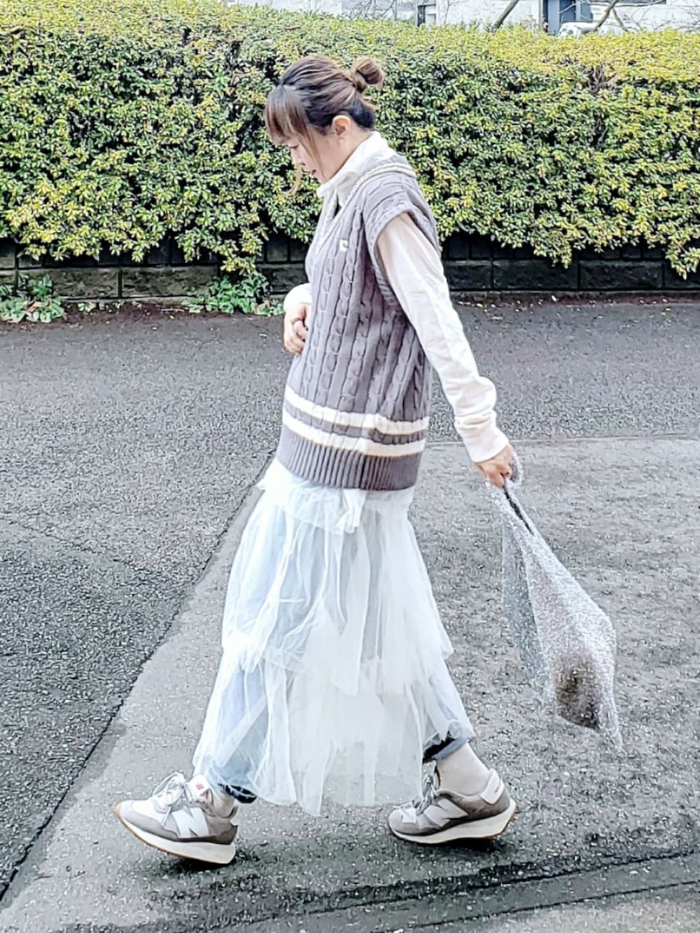 グレー系のベスト、ホワイト系のスカート、ブルー系のデニムパンツを着用したレディースの春コーディネートの2枚目の写真