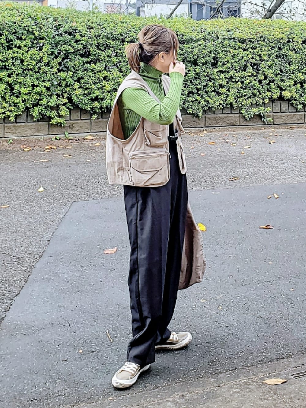 ブラウン系のベスト、グリーン系のニット/セーター、ブラック系のスラックスを着用したレディースの秋コーディネートの2枚目の写真