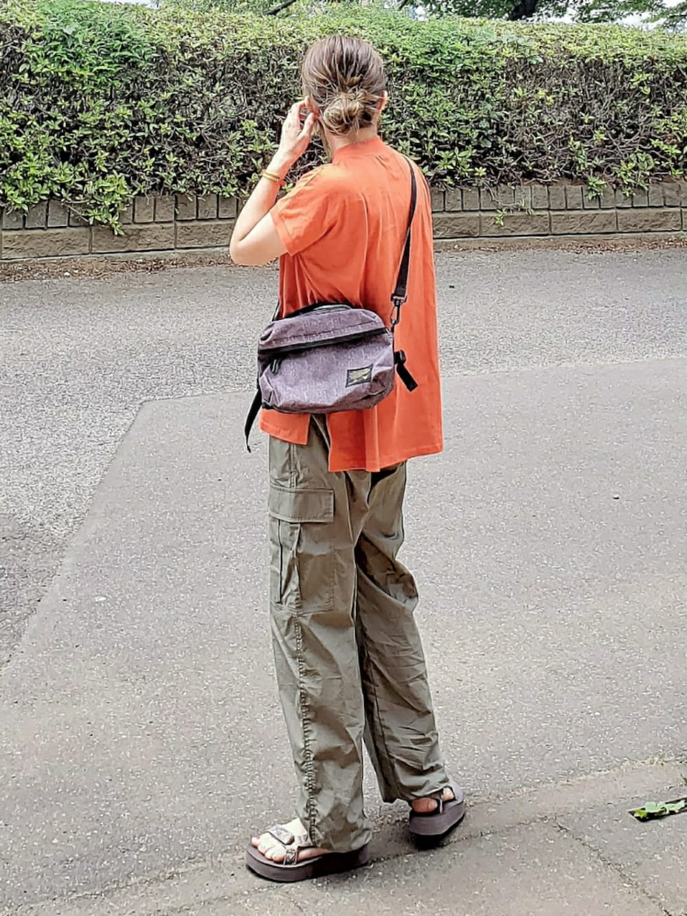 オレンジ系のTシャツ/カットソー、グリーン系のカーゴパンツ、グレー系のショルダーバッグを着用したレディースの夏コーディネートの2枚目の写真