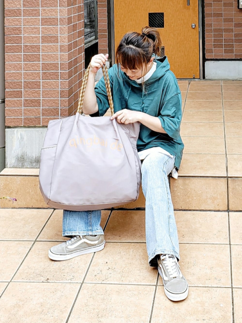 グレー系のトートバッグ、グリーン系のパーカー、ブルー系のデニムパンツを着用したレディースの夏コーディネートの2枚目の写真