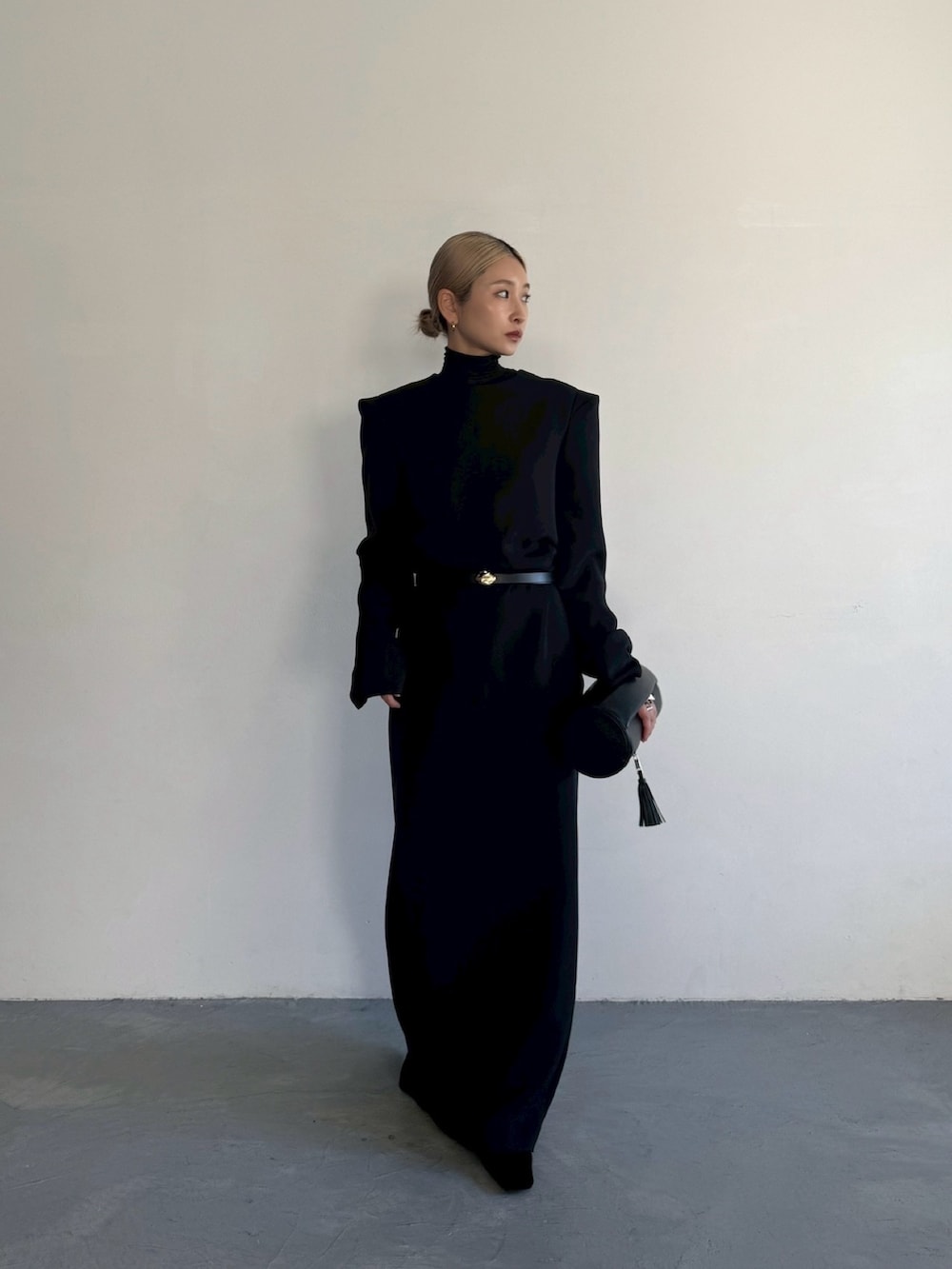 ブラック系のクラッチバッグ、ブラック系のドレス、ゴールド系のベルトを着用したレディースの秋コーディネートの2枚目の写真