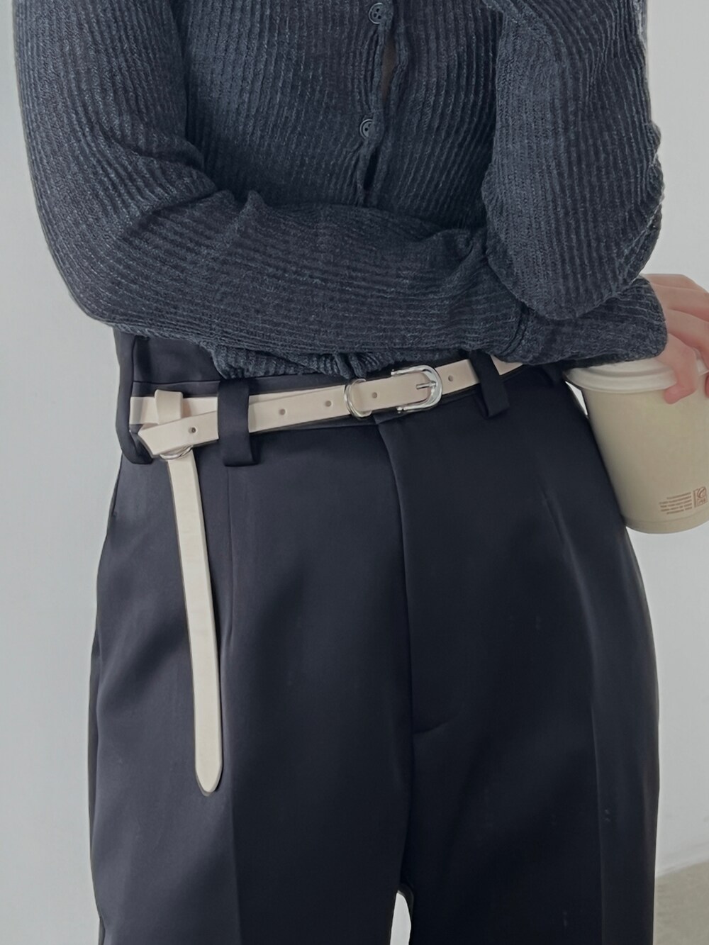 ブラック系のスラックス、グレー系のニット/セーター、ホワイト系のベルトを着用したレディースの冬コーディネートの2枚目の写真