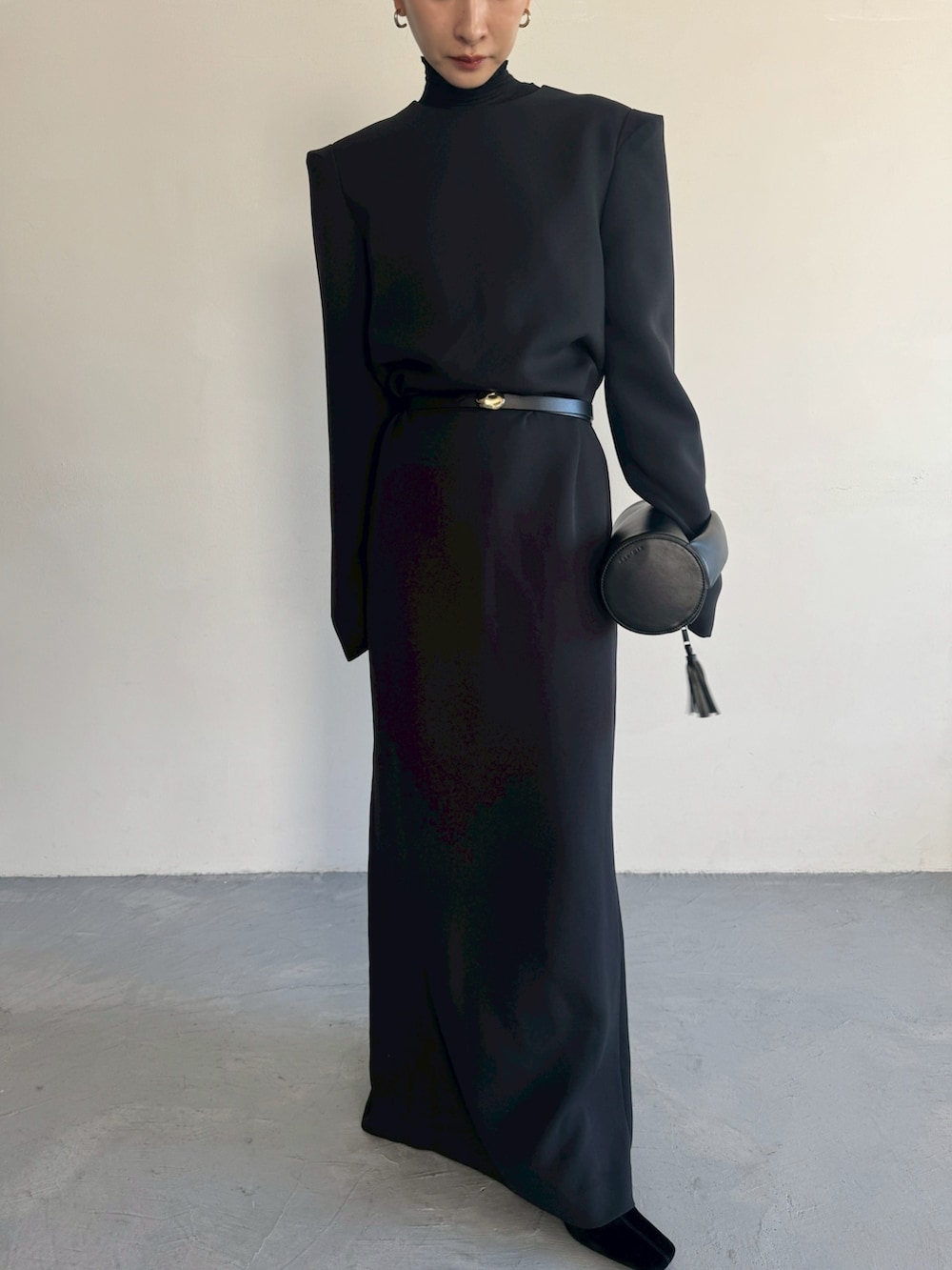 ブラック系のクラッチバッグ、ブラック系のドレス、ゴールド系のベルトを着用したレディースの秋コーディネートの3枚目の写真