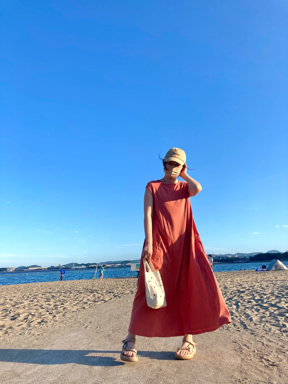 オレンジ系のワンピース、ベージュ系のサンダル、ホワイト系のトートバッグを着用したレディースの夏コーディネートの3枚目の写真