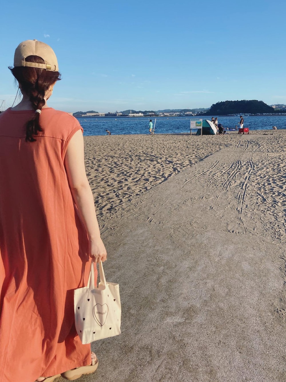 オレンジ系のワンピース、ベージュ系のサンダル、ホワイト系のトートバッグを着用したレディースの夏コーディネートの2枚目の写真