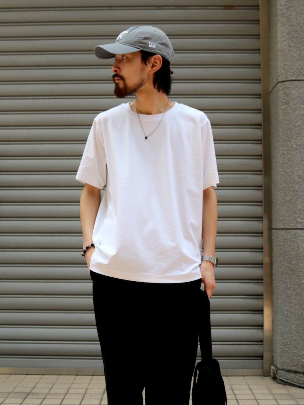 ブラック系のスラックス、ブラック系のトートバッグ、ホワイト系のTシャツ/カットソーを着用したメンズの夏コーディネートの2枚目の写真