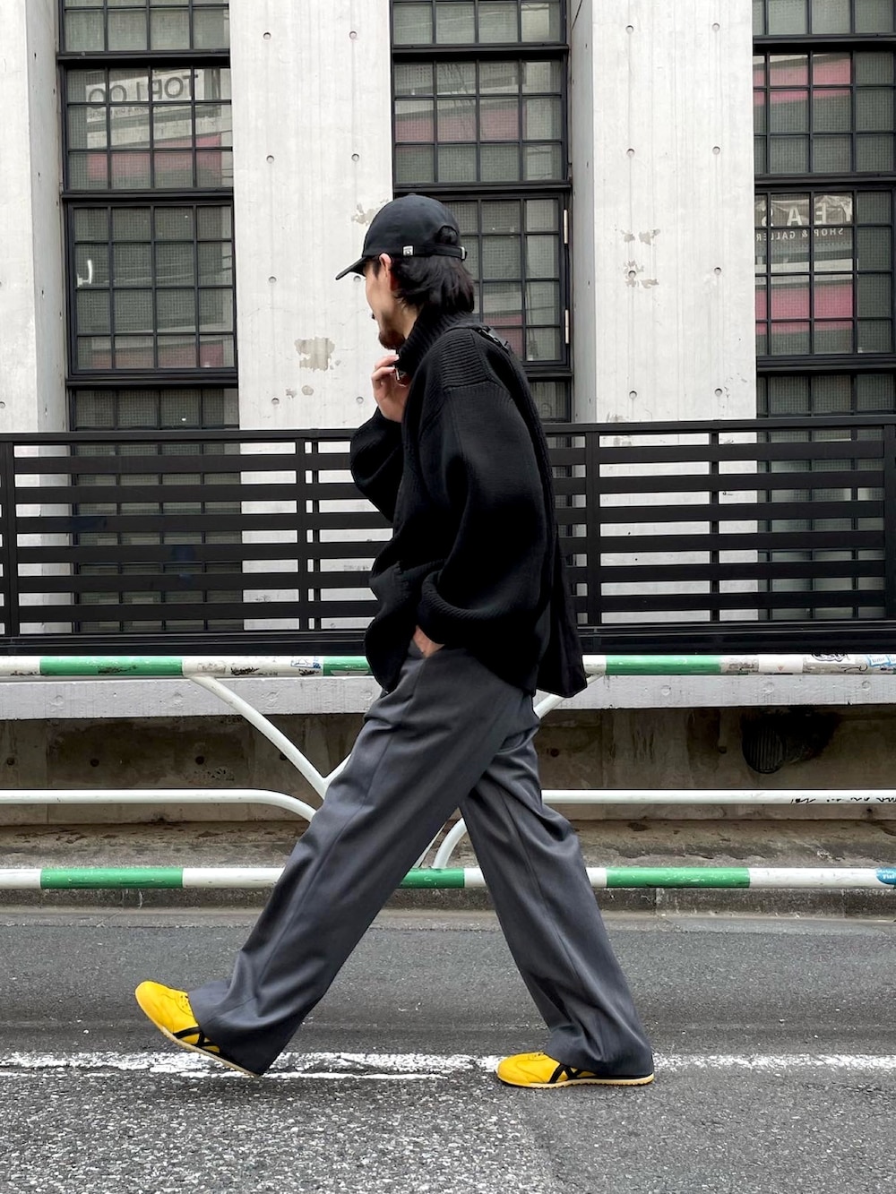 イエロー系のスニーカー、ブラック系のニット/セーター、グレー系のスラックスを着用したメンズの秋コーディネートの2枚目の写真