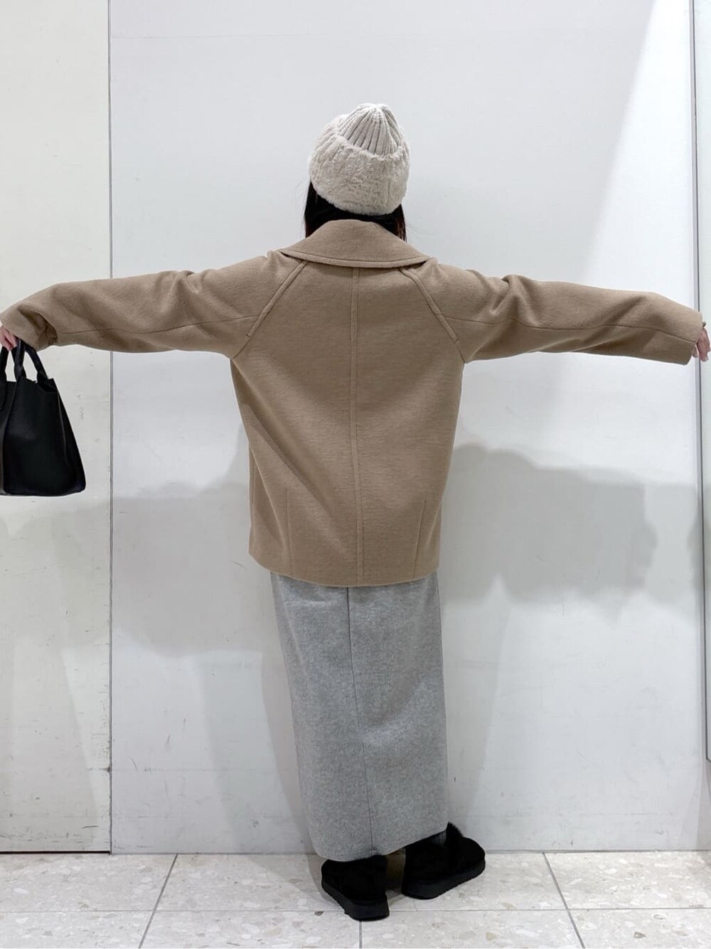 ベージュ系のピーコート、レッド系のカーディガン/ボレロ、グレー系のスカートを着用したレディースの冬コーディネートの3枚目の写真