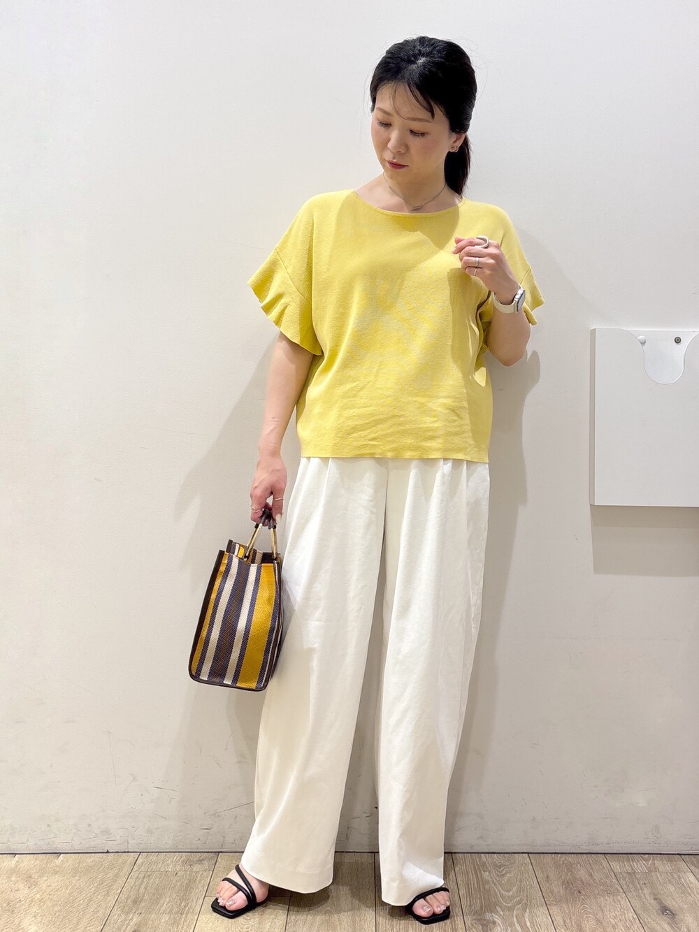 イエロー系のニット/セーター、ホワイト系のその他パンツ、ブラウン系のトートバッグを着用したレディースの春コーディネートの9枚目の写真