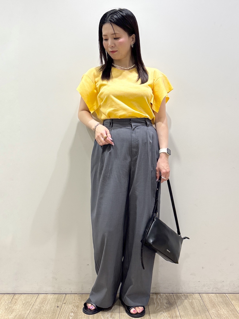 イエロー系のニット/セーター、グレー系のその他パンツ、ブラック系のショルダーバッグを着用したレディースの夏コーディネートの6枚目の写真