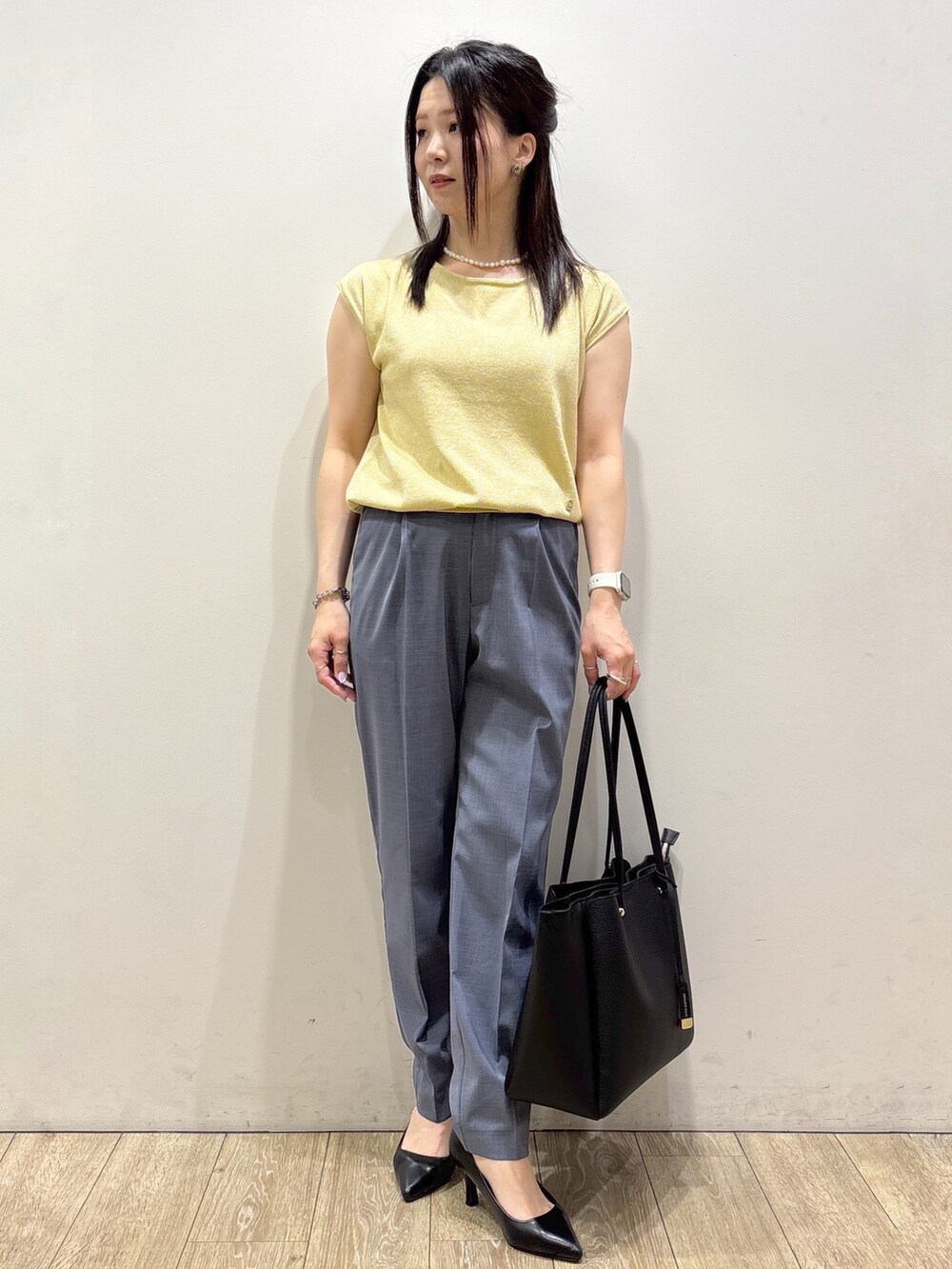 イエロー系のニット/セーター、グレー系のその他パンツ、ブラック系のトートバッグを着用したレディースの夏コーディネートの2枚目の写真