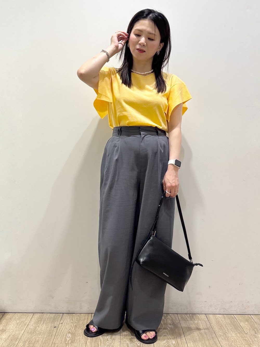 イエロー系のニット/セーター、グレー系のその他パンツ、ブラック系のショルダーバッグを着用したレディースの夏コーディネートの5枚目の写真