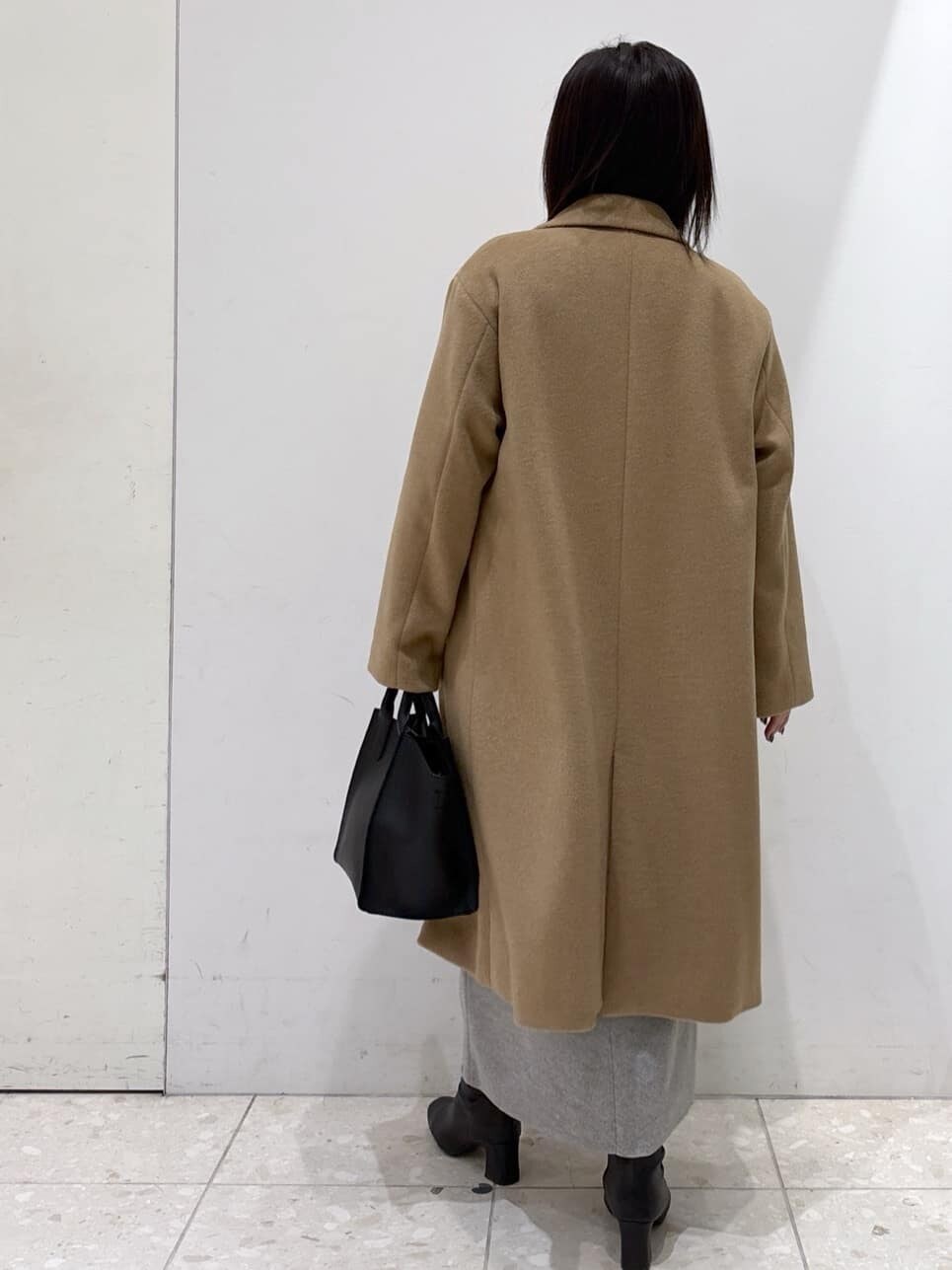 イエロー系のチェスターコート、ベージュ系のニット/セーター、グレー系のスカートを着用したレディースの冬コーディネートの3枚目の写真