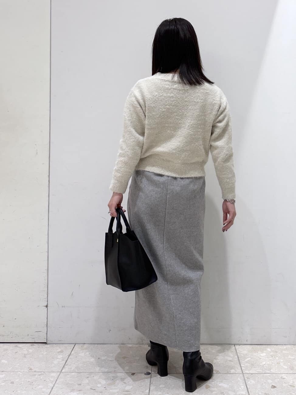 イエロー系のチェスターコート、ベージュ系のニット/セーター、グレー系のスカートを着用したレディースの冬コーディネートの7枚目の写真