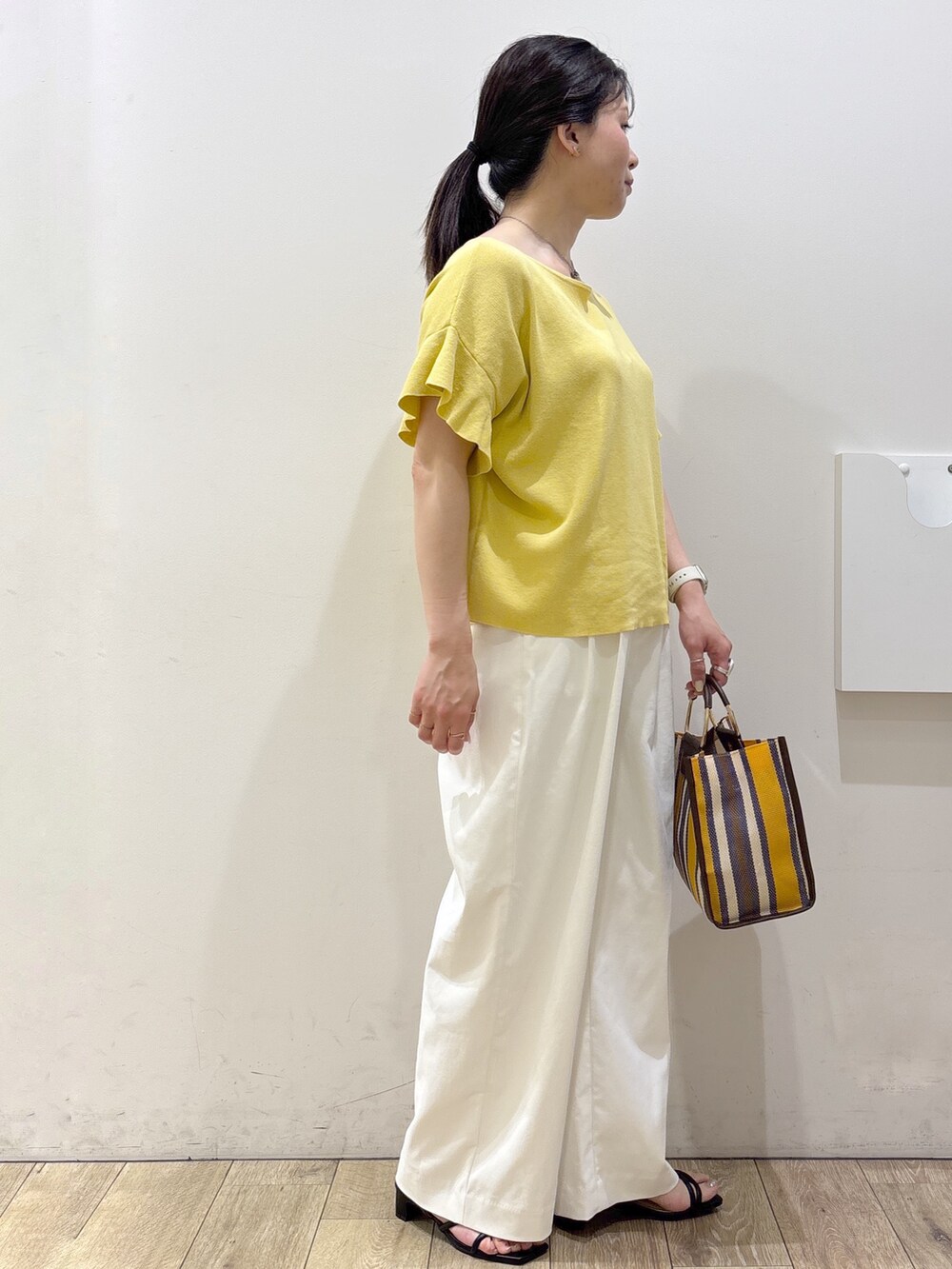 イエロー系のニット/セーター、ホワイト系のその他パンツ、ブラウン系のトートバッグを着用したレディースの春コーディネートの10枚目の写真