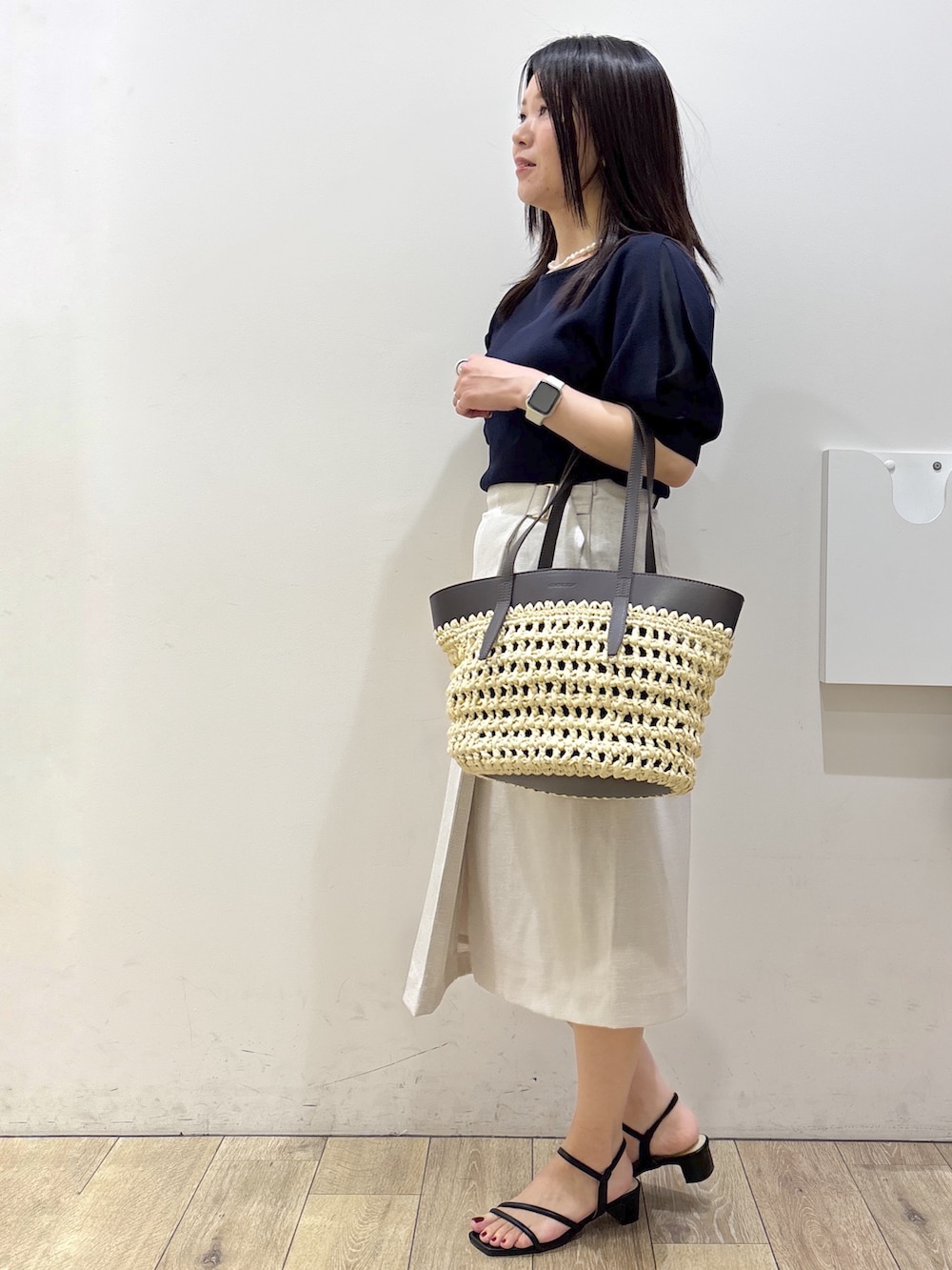 ブルー系のニット/セーター、ベージュ系のスカート、ブラウン系のトートバッグを着用したレディースの夏コーディネートの4枚目の写真